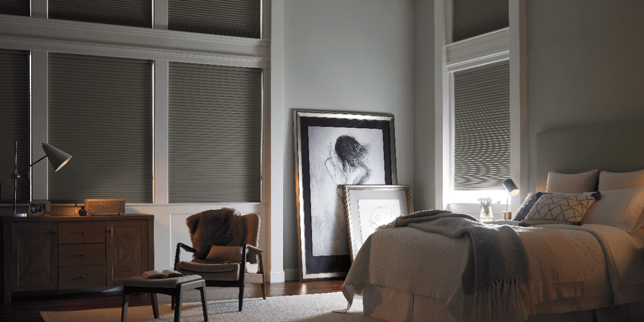 Large, dimly lit bedroom with large windows featuring dark fabric blinds for dramatic lighting. 